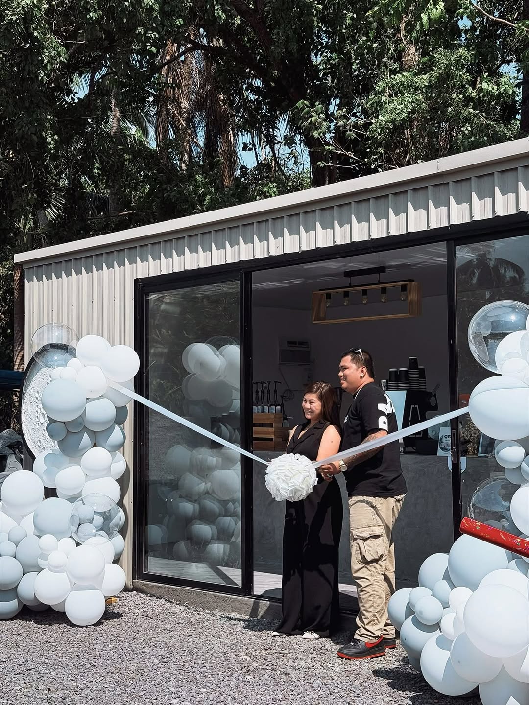The grand opening ribbon-cutting ceremony at Moon Coffee 2.0 — the modern container building with a white balloon arch