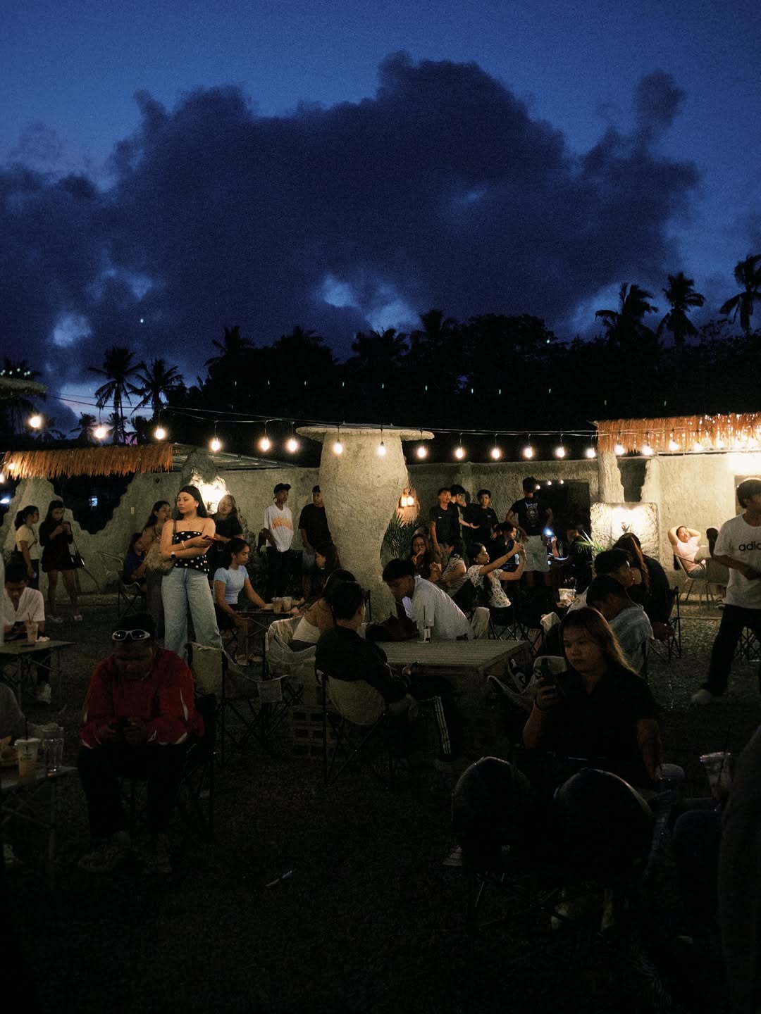 Moon Coffee outdoor seating at blue hour — stone pillars, string lights, coconut palms, and a full crowd